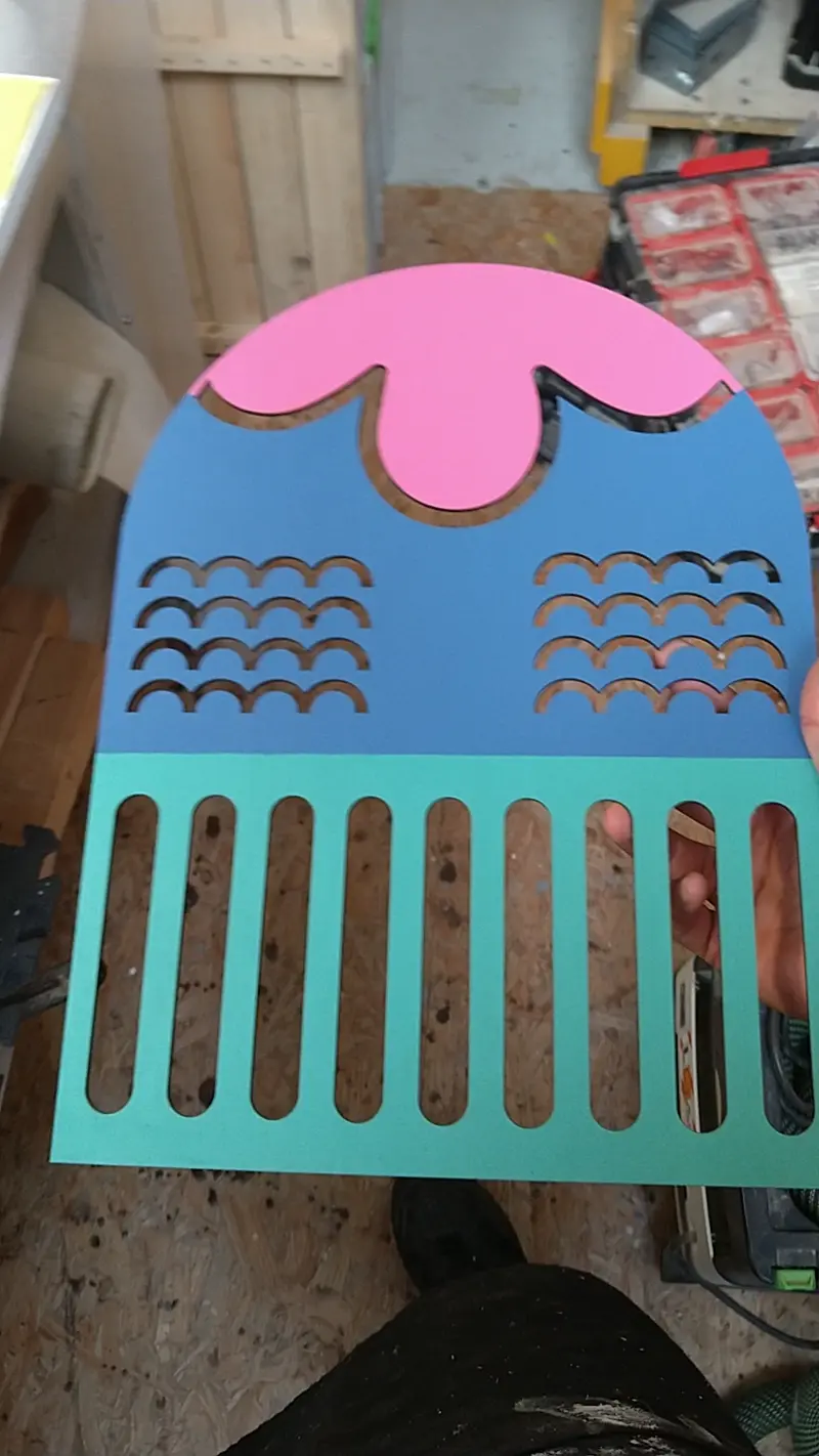 Person lays colourful laser-cut wooden signage over another colourful piece of plywood.