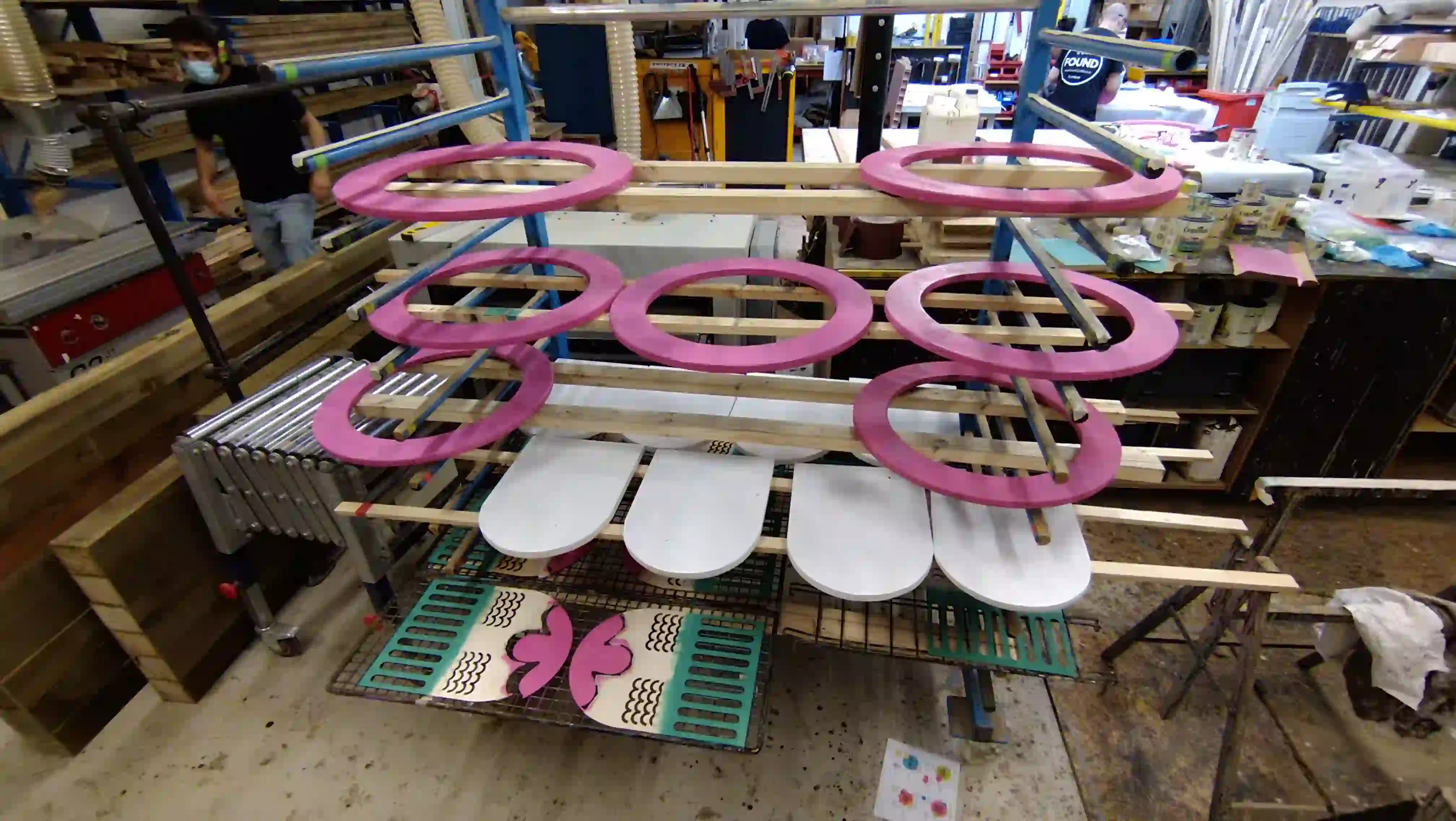 Lots of colourful freshly-painted wooden pieces drying on a drying rack.