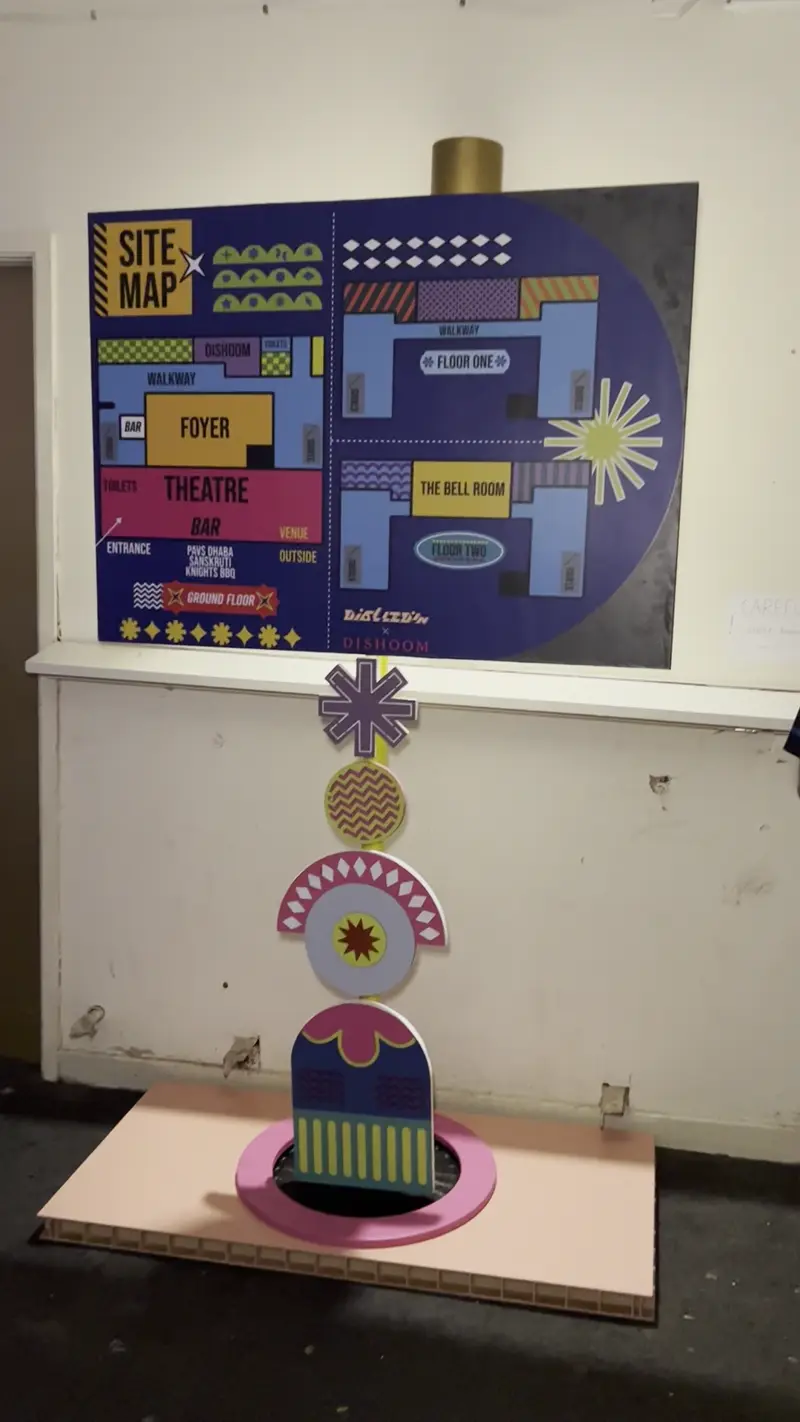 Video displaying a signage at an indoor festival, the camera pans towards the other side of the venue, where people are playing a board game.